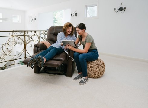 A Happy Woman On A Brown Pride® Power Lift Recliner Next To Her Daughter Who Is Sitting Next To Her
