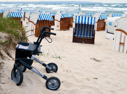 A black rollator parked in the sand, the ocean in the background.