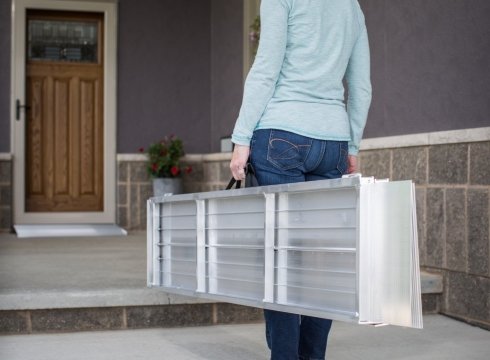 A woman carrying a portable ramp at the entrance of a house