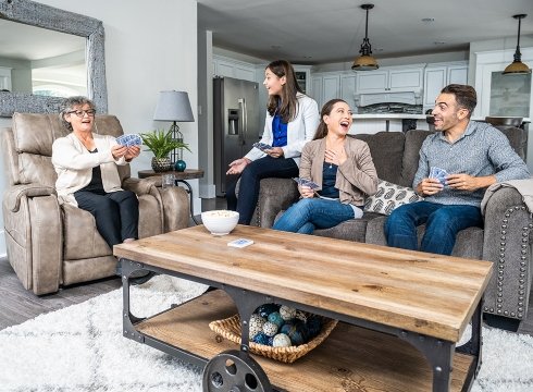 A happy family playing cards in the living room while the oldest family member is sitting on a VivaLift!® lift chair